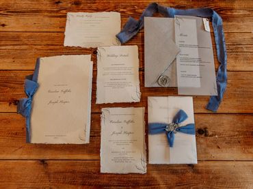 Wedding Invitation set with a vellum wrap, blue ribbons and a grey wax seal, lay on wooden table