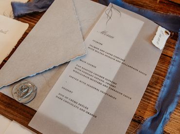 Wedding Invitation set with a vellum wrap, blue ribbons and a grey wax seal, lay on wooden table