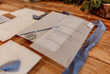 Wedding breakfast place menu with blue ribbons and a grey wax seal, lay on wooden table