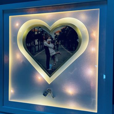 White Picture Frame of a married couple, with a silver key and back lights lights at dusk