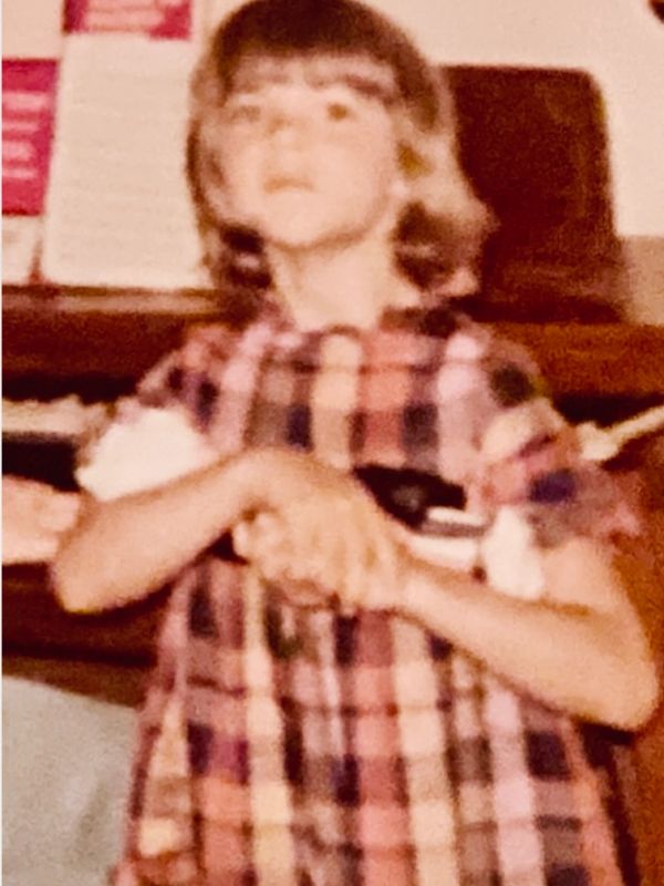 Young girl in a checkered dress posing indoors.