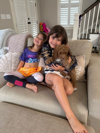 Two children sitting on a couch with a small brown dog.
