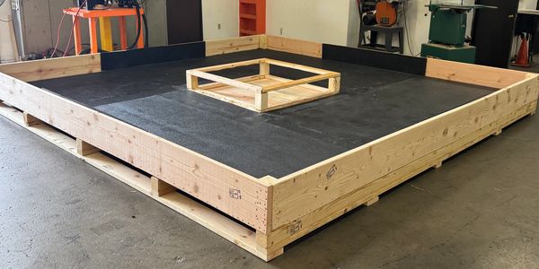 Large wooden frame structure on a workshop floor with a smaller wooden frame inside.