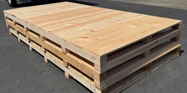 Stack of wooden pallets on a paved surface under sunlight.