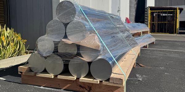 Large metal rods stacked and wrapped on a wooden pallet outdoors.