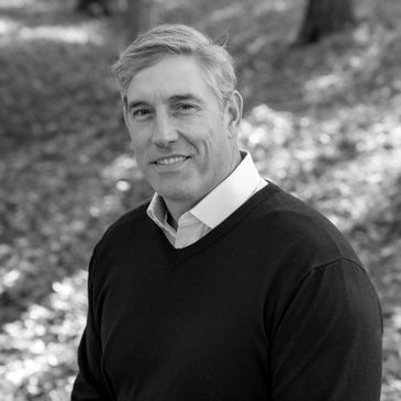 A middle-aged man smiling outdoors in a black and white photo.