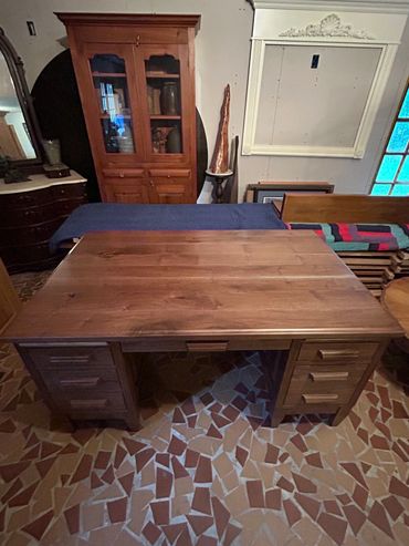 Large wooden desk with drawers in a room with wooden furniture and tiled floor.
