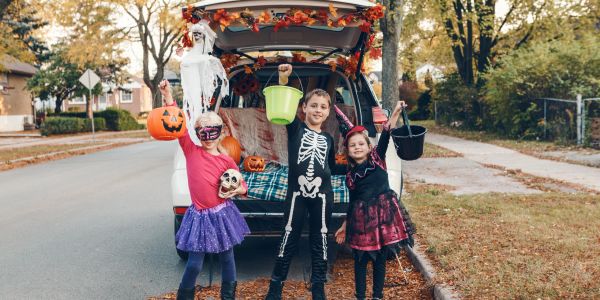 Three children in Halloween costumes holding buckets, ready for trick-or-treating.