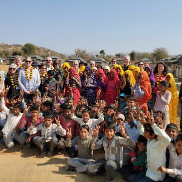 A large group of children and adults posing outdoors in a sunny rural setting.
