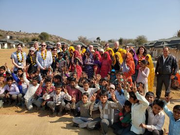 A large group of children and adults posing outdoors with smiles and peace signs.