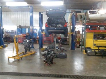 Car lifted in garage with a mechanic doing an engine replacement.