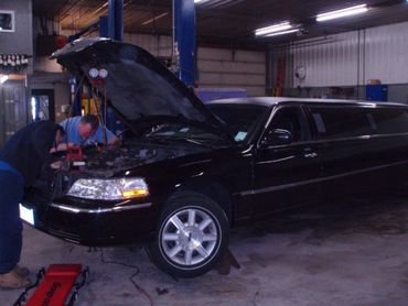 Mechanics working on a black limousine in a garage with the hood open.