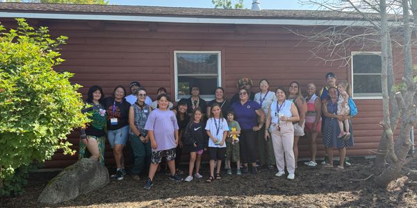 A large group of people posing outdoors in front of a wooden building.