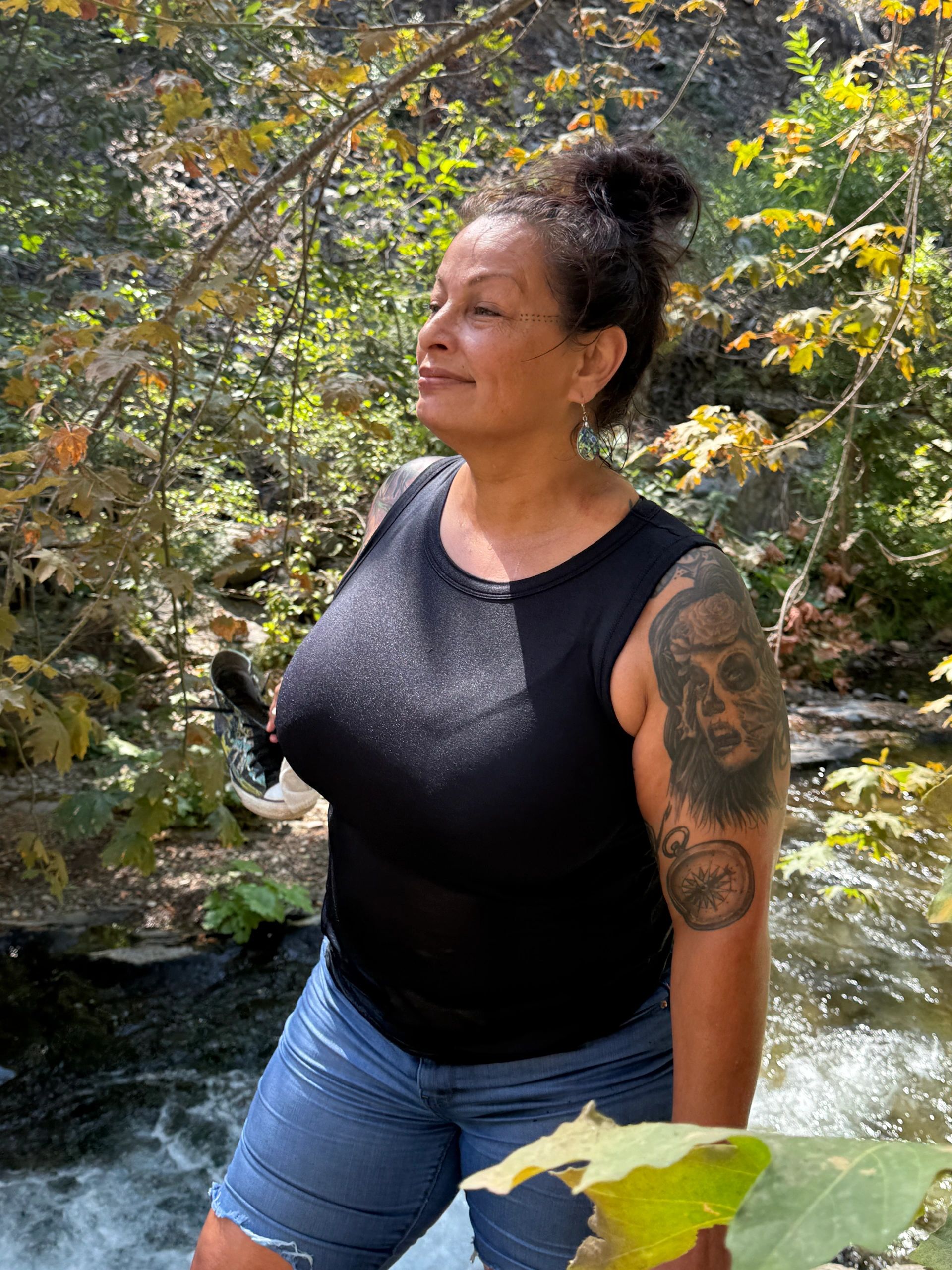 Woman with tattoos enjoys a sunny day by a river in the woods.