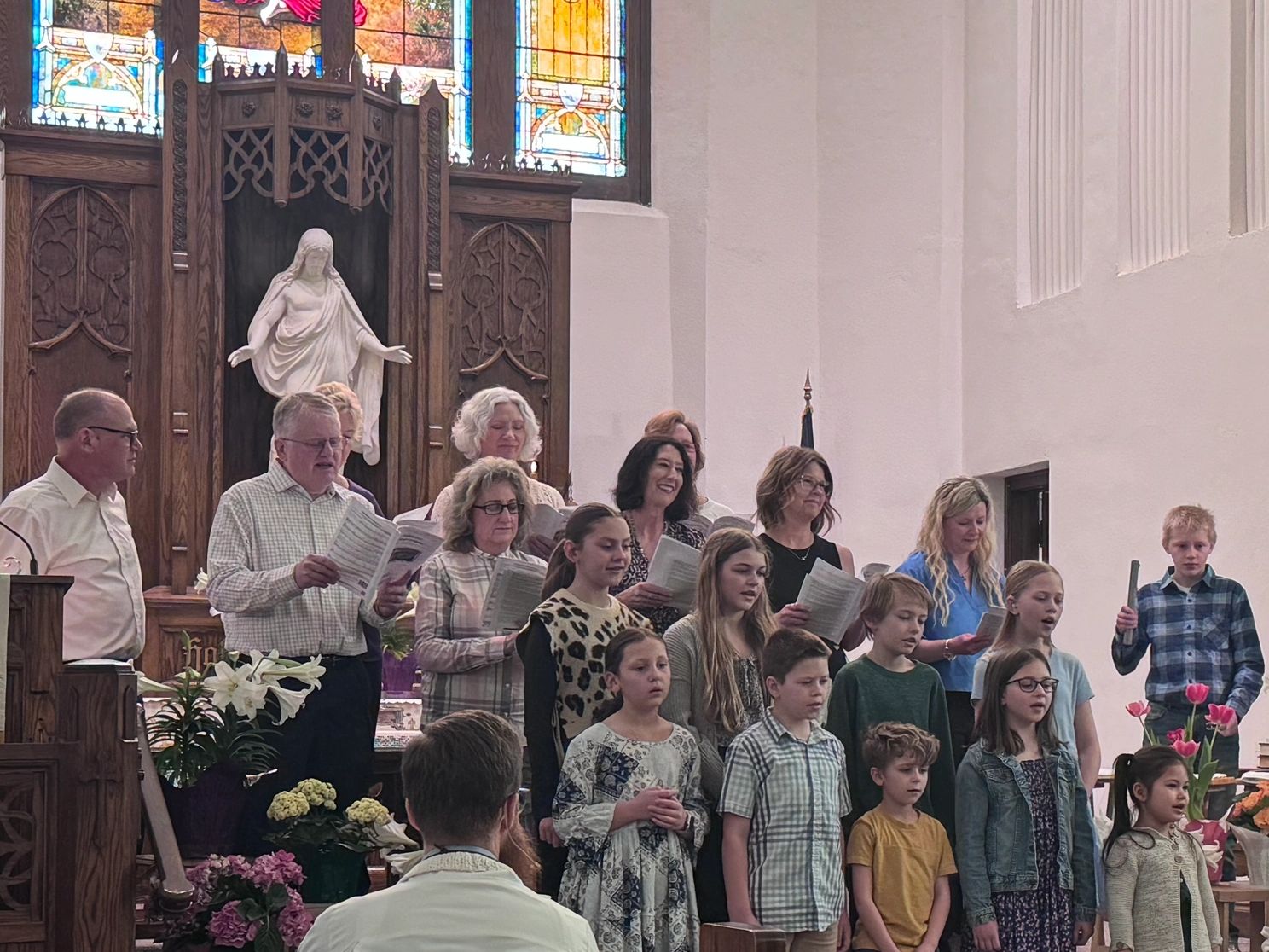 Group singing in a church with stained glass and flowers.