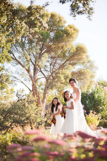 Bride with two flower girls in a sunlit garden.