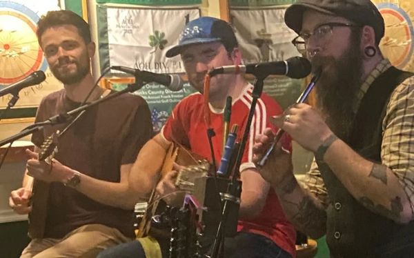 Three musicians playing instruments and singing in a cozy setting.