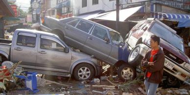 Man walking past cars pushed on top of each other after flooding.  