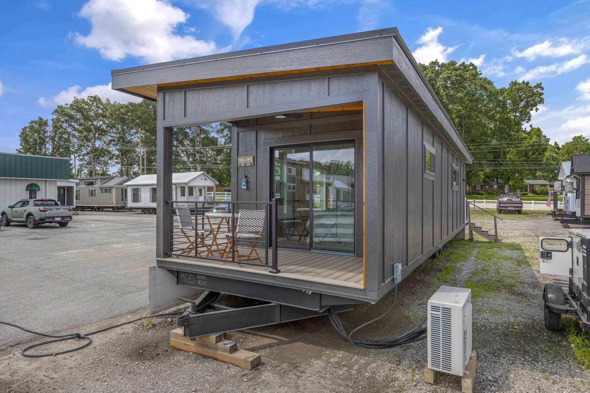 Modern tiny house on wheels with a small porch and outdoor seating.