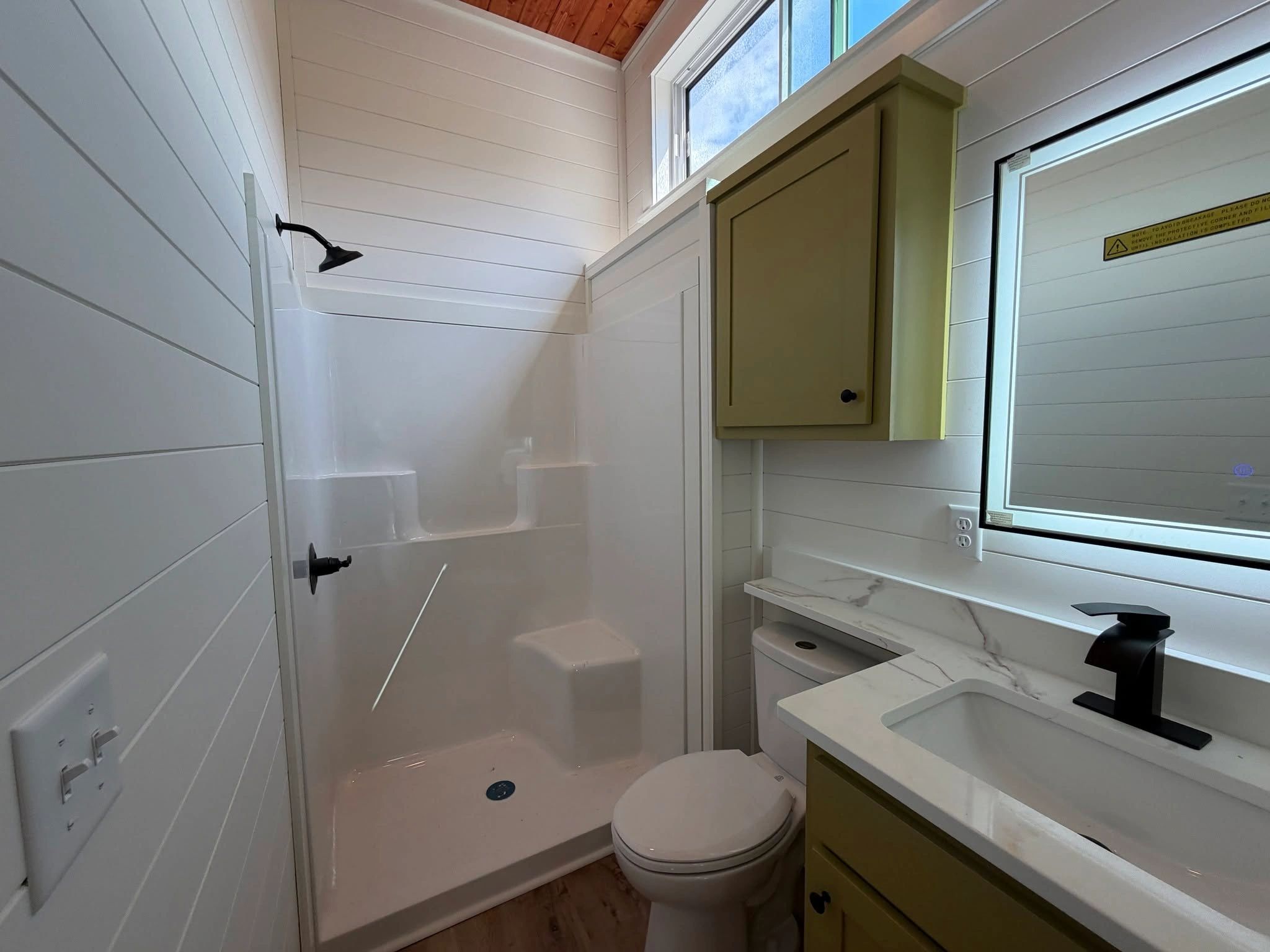 Small modern bathroom with shower and green cabinetry.