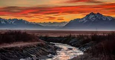 A river flows with mountains under an orange sunset.