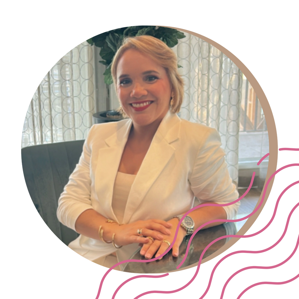 Smiling woman in white blazer sitting at a table indoors.