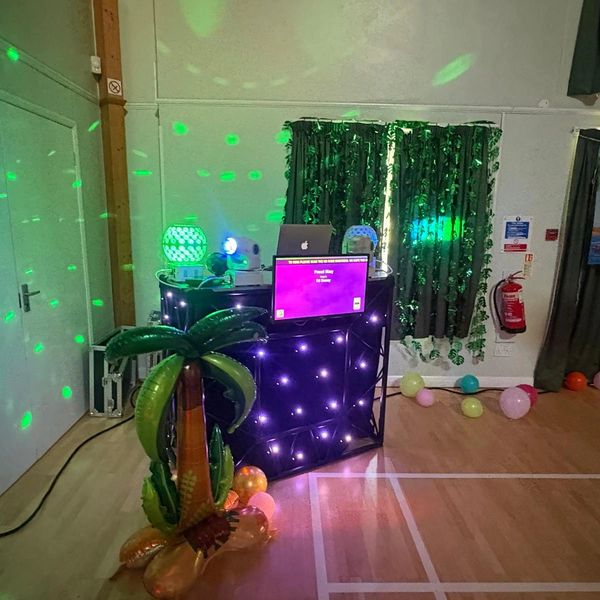 DJ booth with colorful lights and inflatable palm tree at a party.