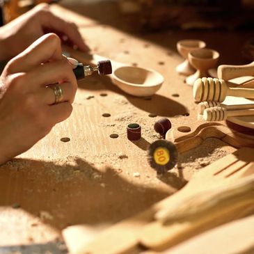 A person sanding wooden spoons with a rotary tool.