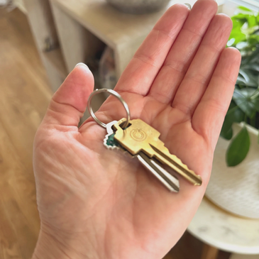 Hand holding a set of keys with a green keychain indoors.