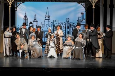 Theatrical group dressed in period costumes on stage.
