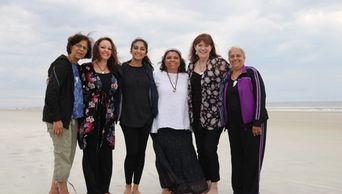 Group of six women standing on a beach.