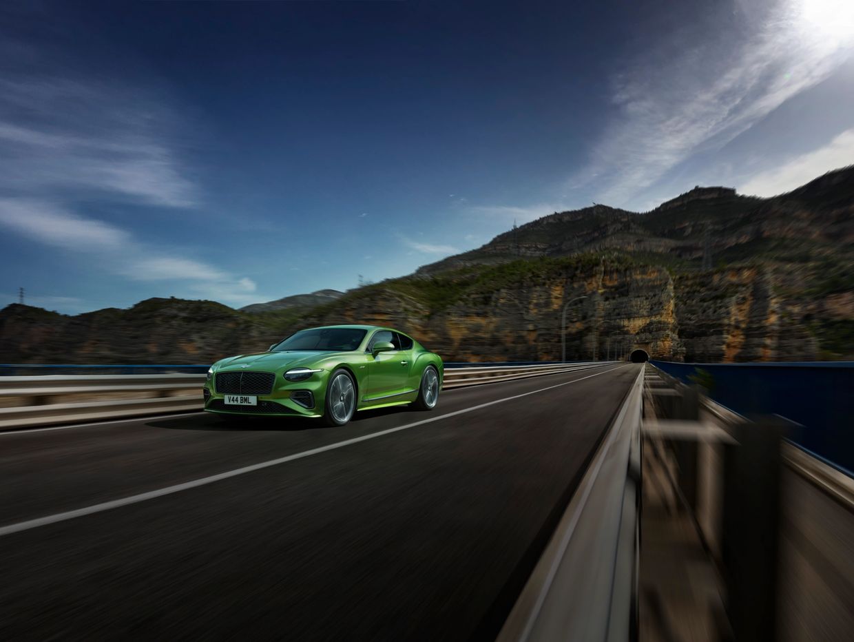 A green sports car driving on a mountain road near a tunnel.