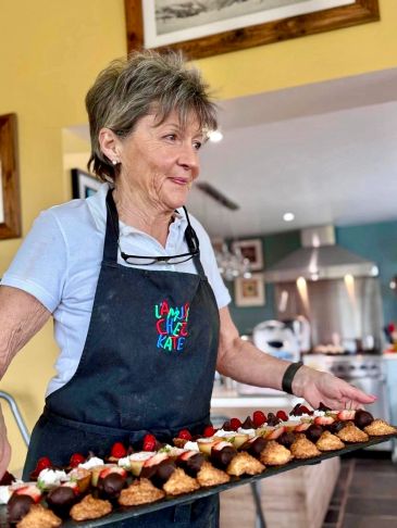 Elderly woman holding tray of desserts.