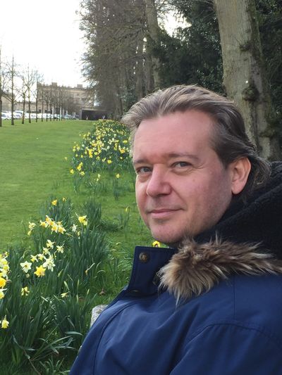 Man in blue coat sitting near blooming yellow daffodils in a park.