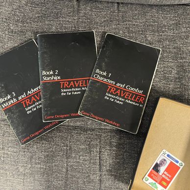 Three vintage Traveller RPG booklets and a boxed set on a gray fabric surface.