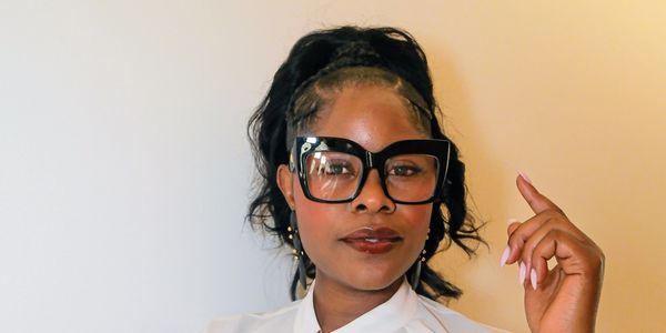 Confident woman in a white blouse and black skirt, wearing large glasses and a black bracelet.