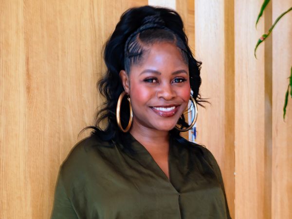 Smiling woman in green blouse and hoop earrings against wooden background.