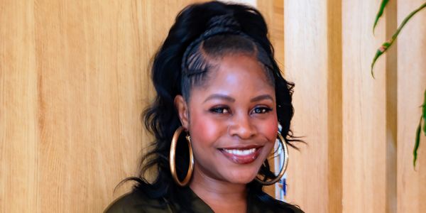 Smiling woman in green blouse and hoop earrings against wooden background.