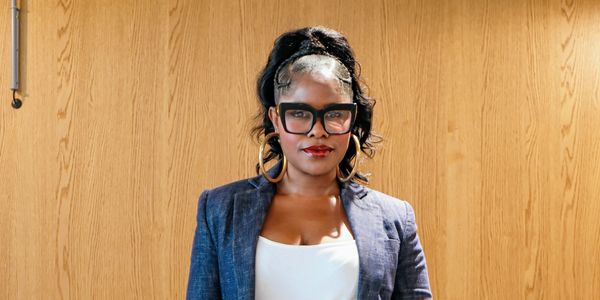 Confident businesswoman standing behind a desk with laptop, tablet, and phone.