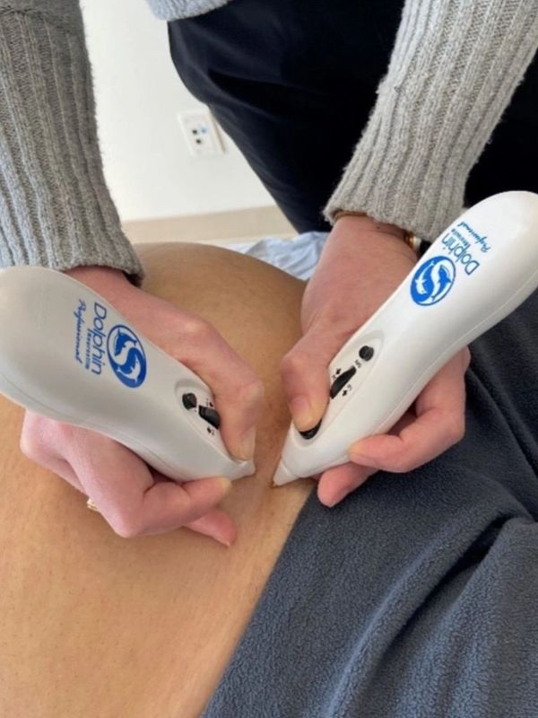 Close-up of hands using Dolphin Neurostim devices on a person's back for therapy.