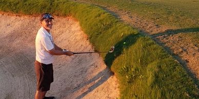 Robert Realmuto smiling with a golf club in a sand trap at sunset.