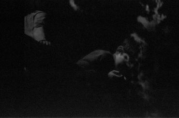 A dark, grainy photo of a person looking down, partially illuminated.