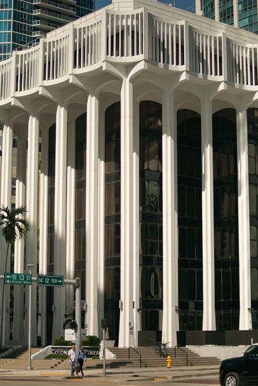 Modern white building with tall columns and large glass windows on a city street corner.