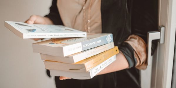 Persona che tiene una pila di libri in mano.