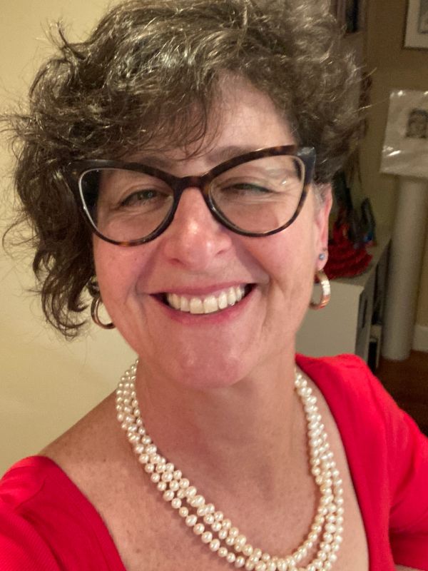 Smiling woman wearing glasses, pearls, and a red top.