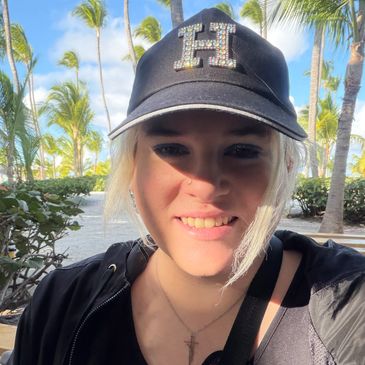 Smiling woman in a black hat outdoors with palm trees.