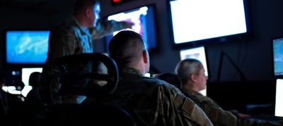 Military personnel monitoring data on multiple screens in a dark room.