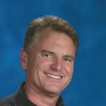 Smiling man with short brown hair against a blue backdrop.