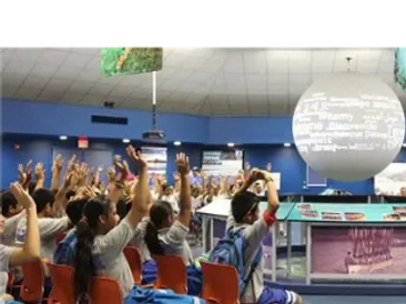 Students raising hands in an interactive classroom with a large globe display.