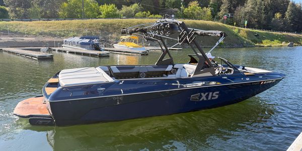A sleek black Axis wakeboard boat docked on calm water.